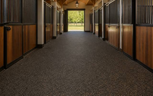 Dark brown rubber surfacing running down a horse barn aisle between stalls