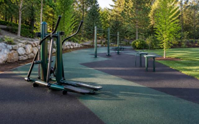 Green and black rubber surfacing under a row of outdoor fitness equipment