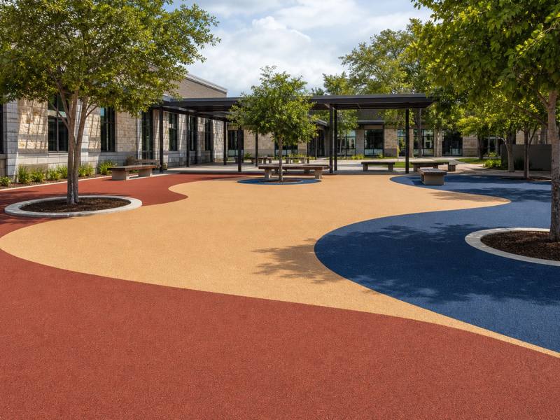 Red and tan rubber surfacing around planted trees in a Sudbury school courtyard